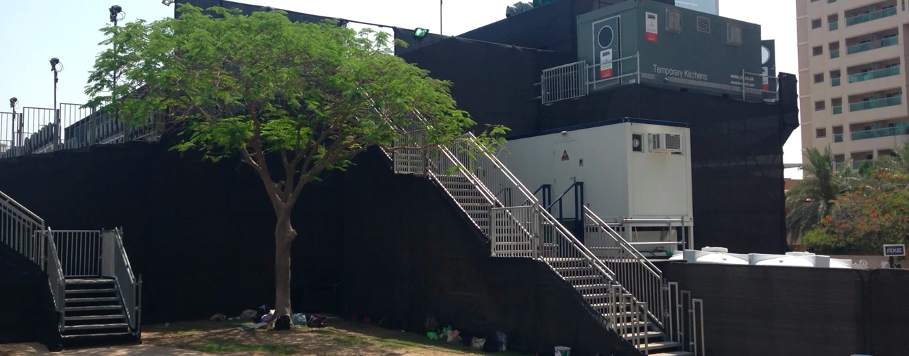 Corporate hospitality kitchens at Dubai Rugby Sevens, featuring a metal staircase and green tree.