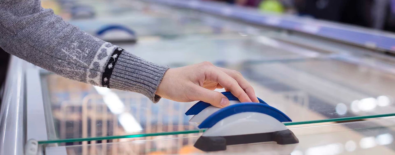 A hand gently touches a blue and white object on a glass surface, with blurred background elements.