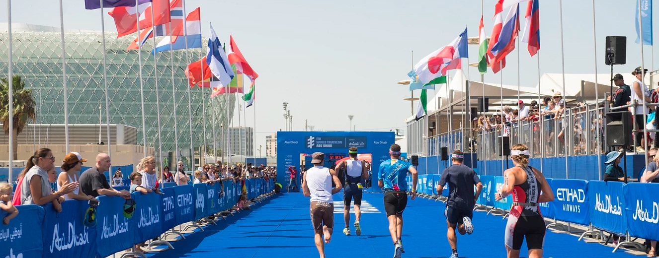 Athletes in sports attire run on a blue track, with flags from various countries in the background.