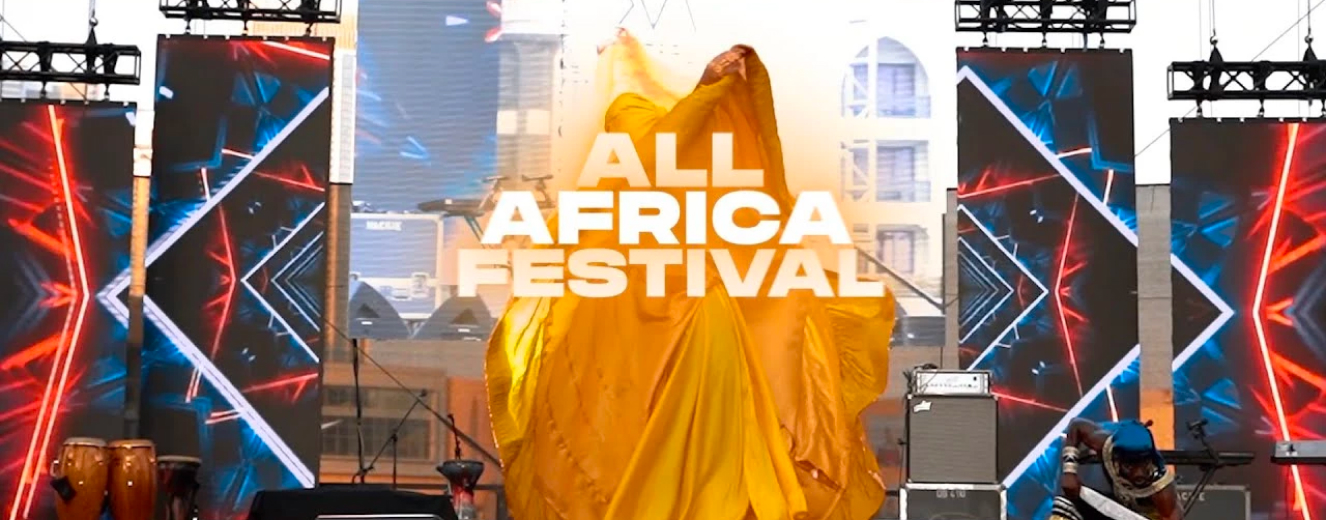 A performer in a flowing yellow costume captivates the audience at the All Africa Festival.