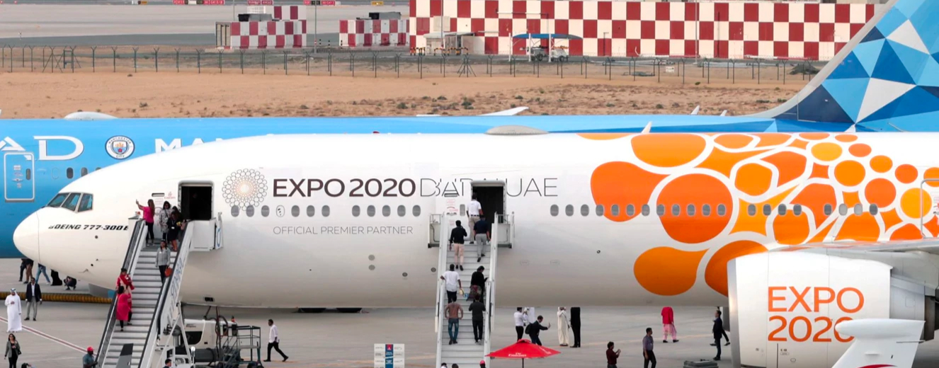 A large aircraft with an orange logo and "EXPO 2020 Dubai UAE" text, parked at an airshow.