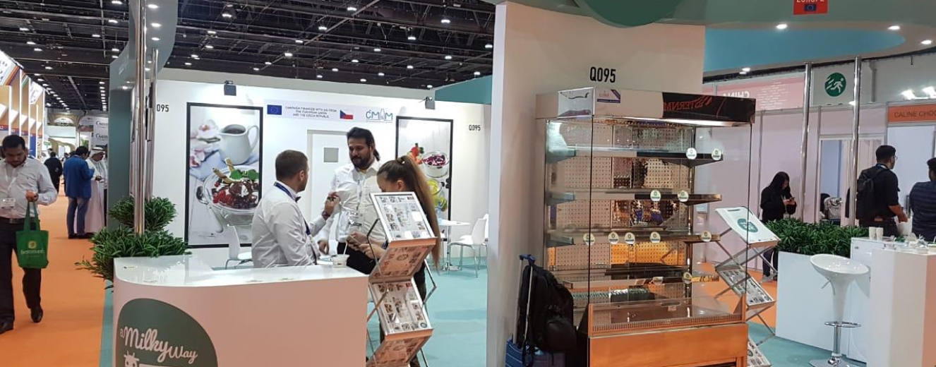 Three people engage at a trade booth featuring white displays and a glass showcase at SIAL Middle East.