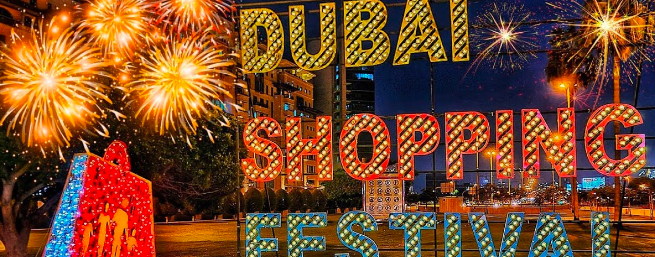 Brightly lit sign reading "DUBAI SHOPPING FESTIVAL" with colourful lights and fireworks in the background.