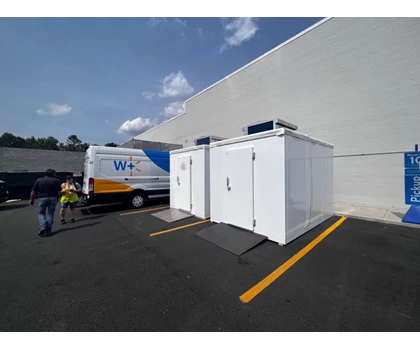 Two white storage units beside a parked van, with a blue sky and scattered clouds above.