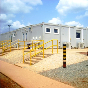 Large white modular kitchen building with yellow railings, set against a blue sky and sandy ground.