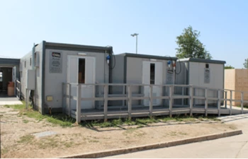 Three grey modular buildings with wooden ramps, set against a clear blue sky.