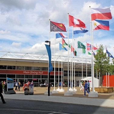 A row of flags in various colours outside a large building with a modern design.