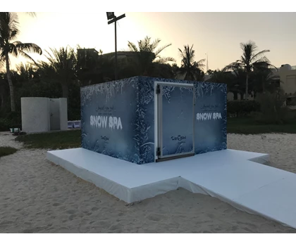 A large blue container with "FRESH DNA" signage, situated on sandy ground with palm trees in the background.
