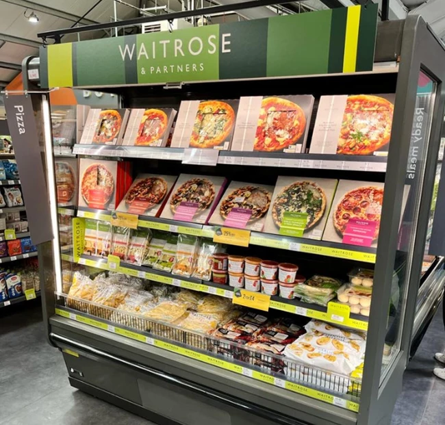 Waitrose display featuring various packaged meals, predominantly in vibrant colours, in a grocery store.