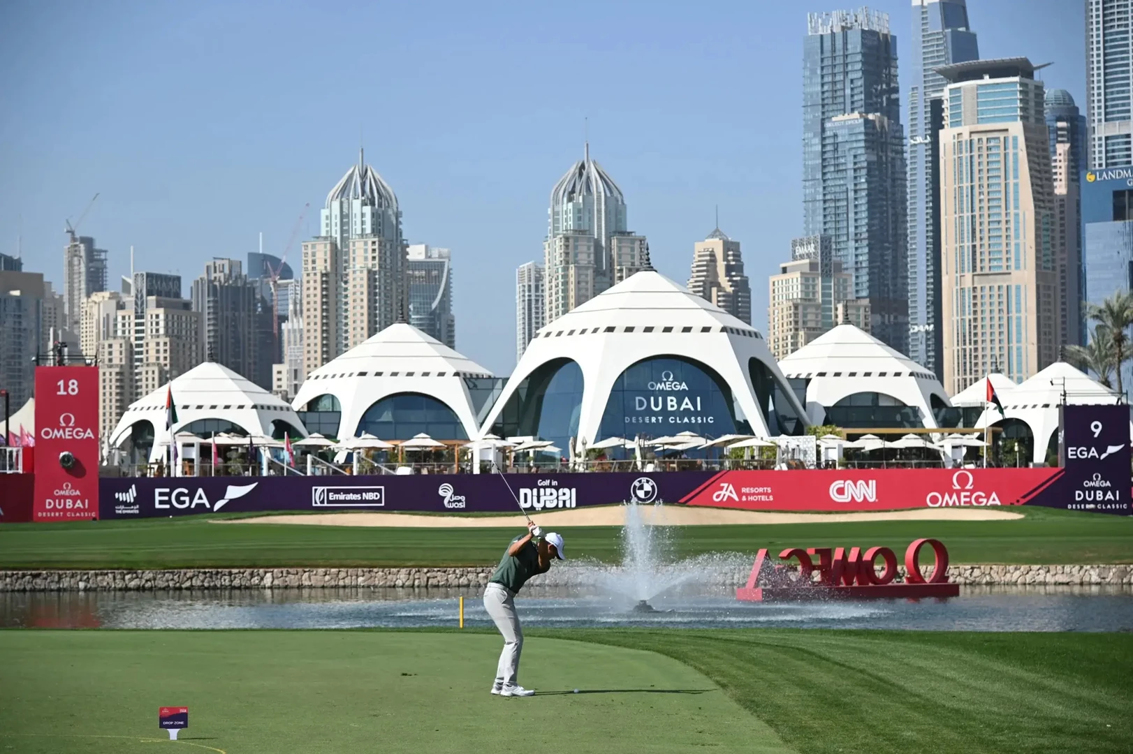 A golfer swings on a lush green course with modern Dubai skyscrapers in the background.