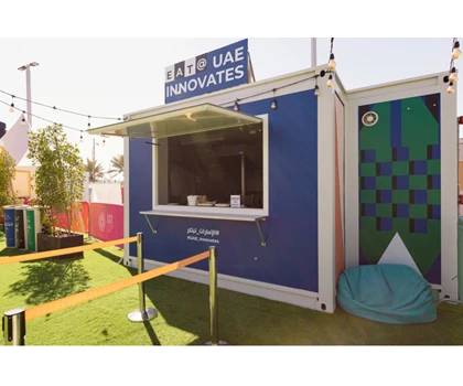Blue container labelled "UAE Innovates" with a green patterned wall and outdoor seating area.