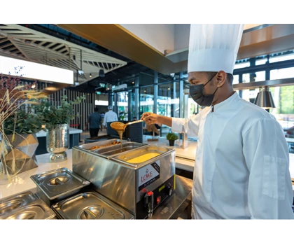 A chef in a white uniform and hat prepares food at a modern kitchen station.