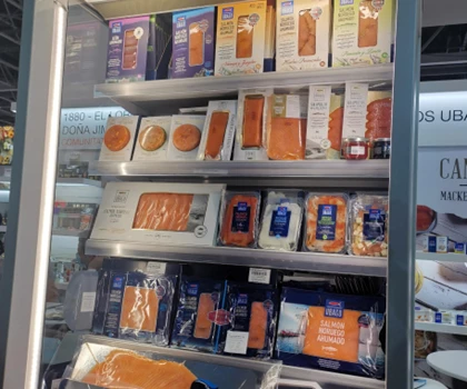 Display of various orange-packaged food products arranged on shelves in a refrigerated unit.