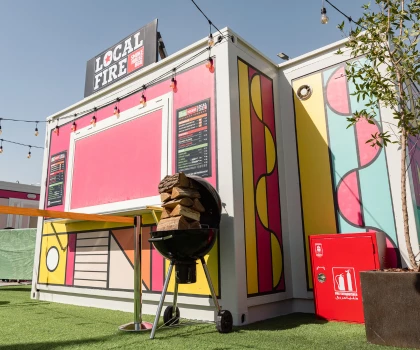 Brightly coloured temporary kitchen with pink and yellow patterns, featuring a grill and signage.