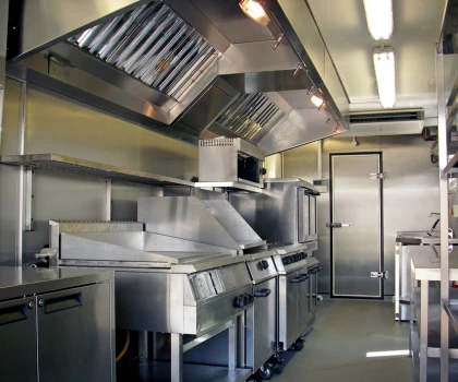 Modern temporary kitchen with stainless steel appliances and grey flooring, featuring ventilation hoods and a door.