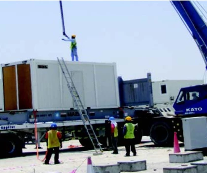 Workers in safety vests oversee the unloading of a large container from a truck.