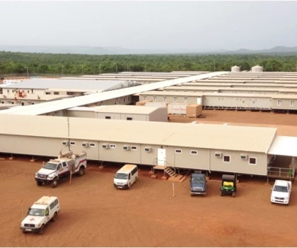Aerial view of beige modular buildings on red soil, with several parked vehicles nearby.