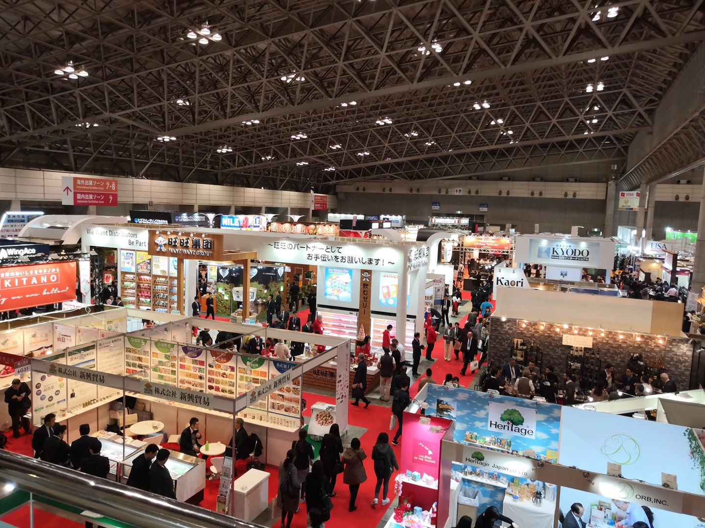 Busy exhibition hall with red carpet, featuring various booths and attendees exploring short-term rental options.