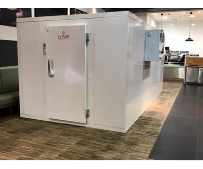A large white structure with a door, set on a textured brown floor in an event space.