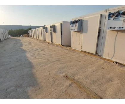 Row of white refrigerators lined up on a sandy surface under a clear sky.