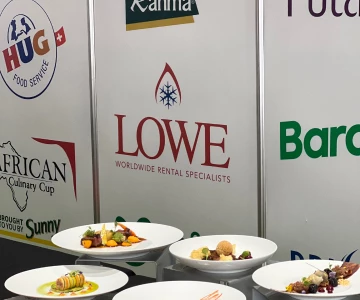Plates of colourful dishes displayed in front of branded banners, featuring the Lowe logo prominently.