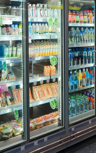 Refrigerated display showcasing various drinks and snacks, featuring vibrant packaging and clear glass doors.