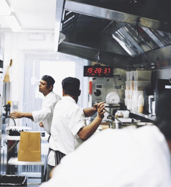 Chefs in white uniforms work in a bright, temporary kitchen with stainless steel appliances.