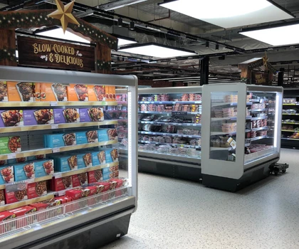 Brightly lit supermarket aisle featuring multiple ice cream freezers with colourful packaging.