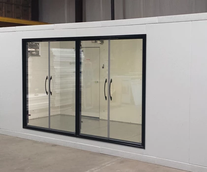Modern white container with large glass doors and black frames, set against an industrial background.