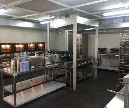 Modern kitchen with stainless steel equipment, grey flooring, and illuminated workspaces.