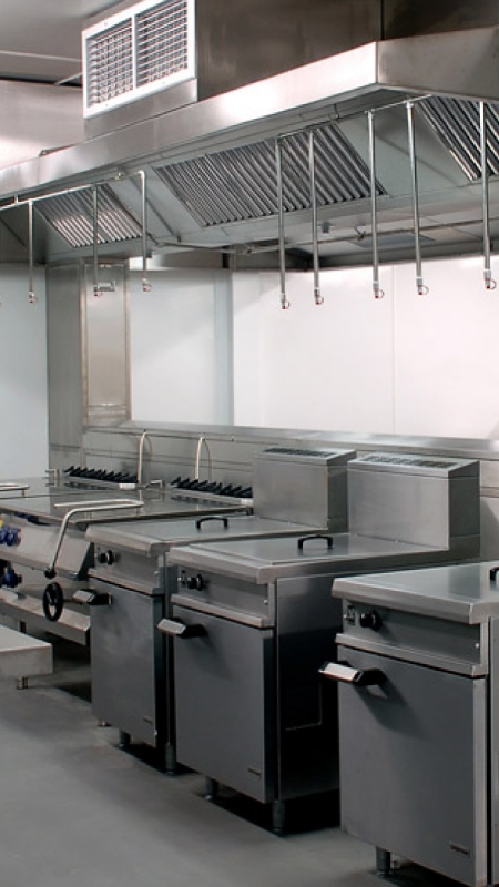Stainless steel kitchen equipment, including fryers and grills, arranged neatly against a white wall.
