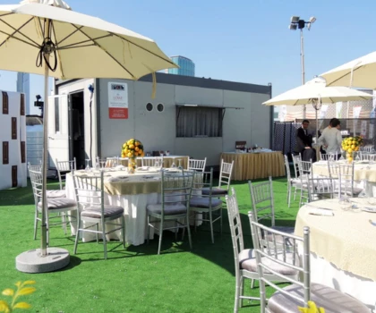 Temporary kitchen setup with white tables and chairs, surrounded by green grass and umbrellas.