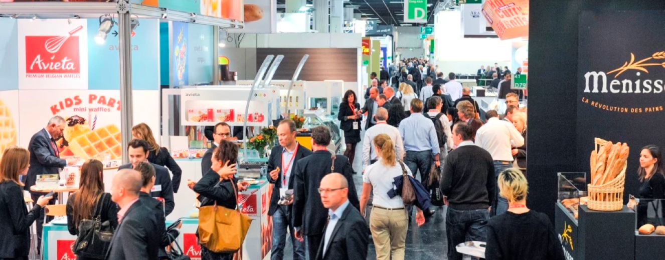 Busy exhibition hall with diverse attendees, featuring bright displays and a modern, polished environment.