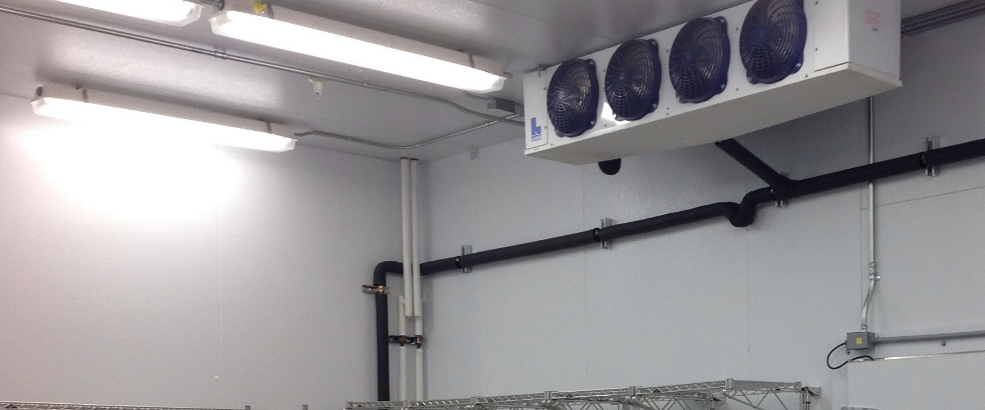 White walls with grey pipes and a cooling unit featuring blue fans in an industrial setting.