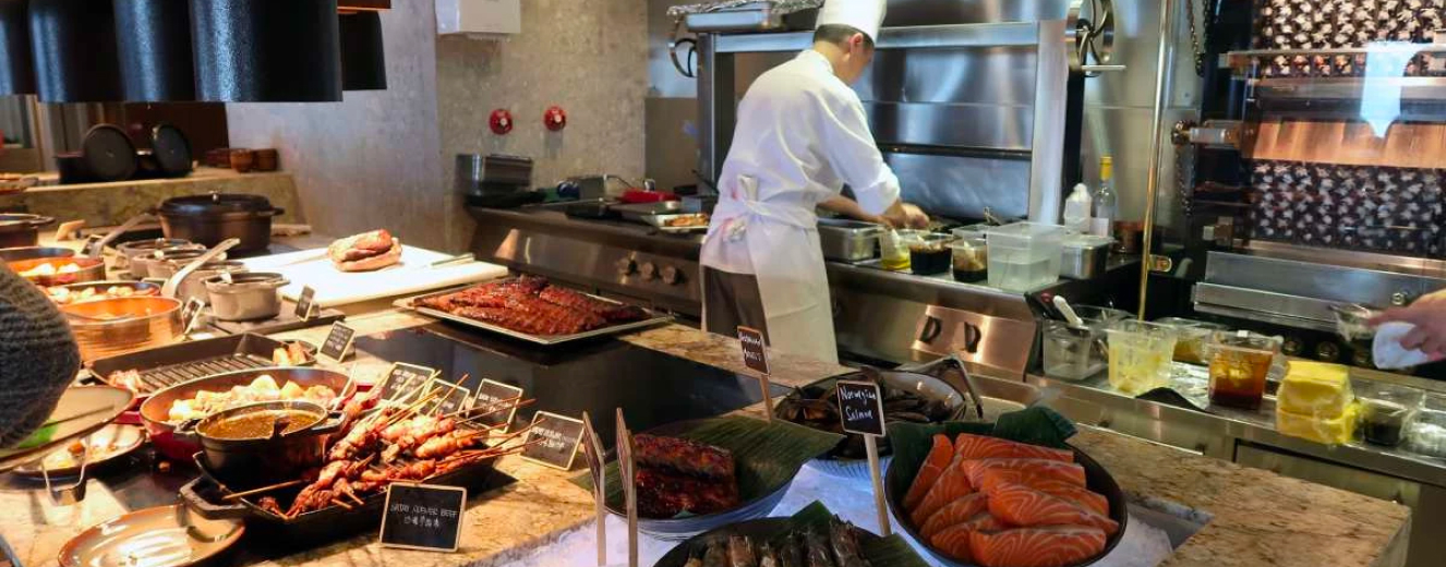 A chef in a white uniform prepares dishes at a buffet featuring vibrant seafood and meats.