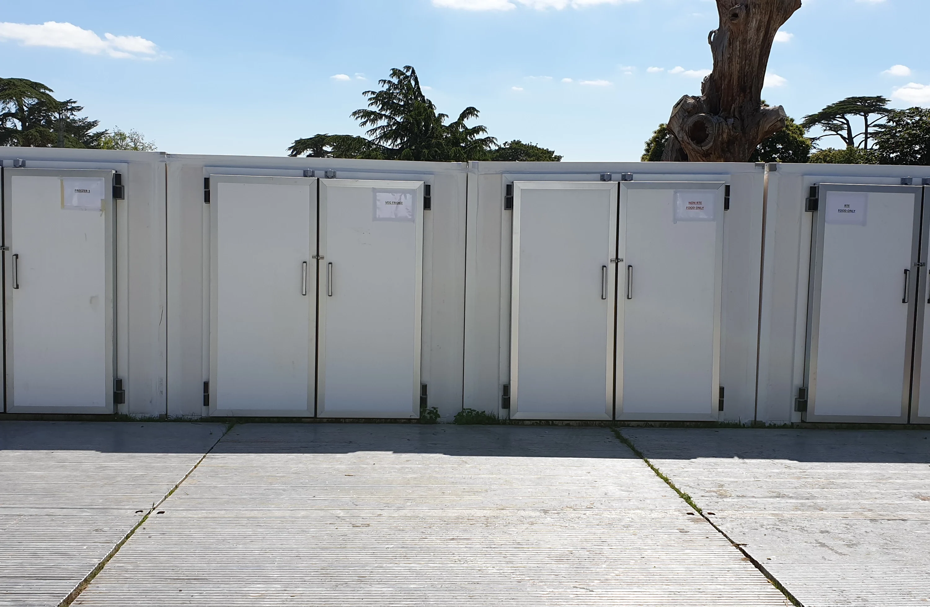 Four white storage doors lined up against a bright blue sky and palm trees in the background.