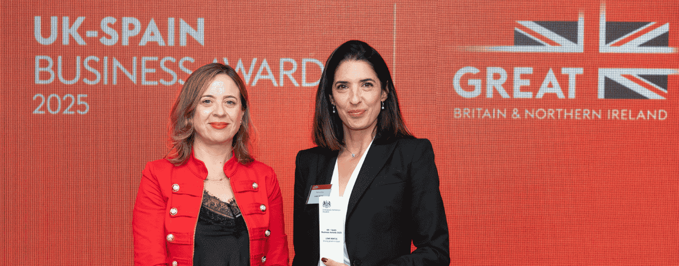 Two women pose together, one in a red jacket and the other in a black suit, against a red backdrop.