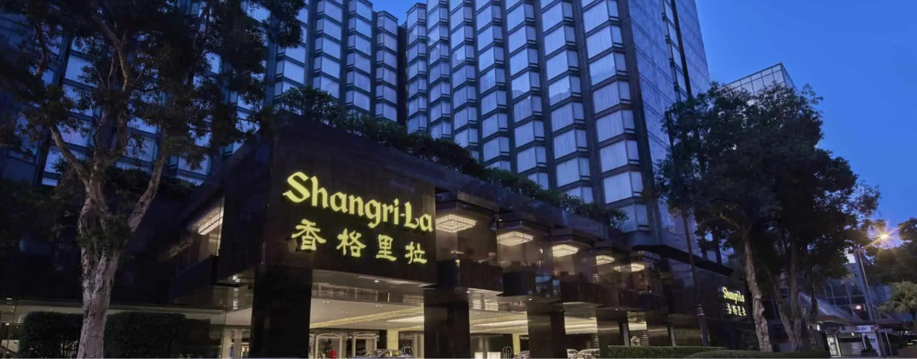 Shangri-La hotel exterior at dusk, featuring illuminated signage and modern glass architecture.