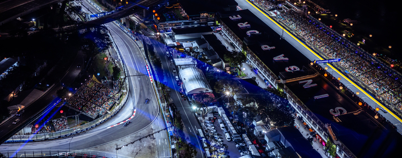 Aerial view of a racetrack illuminated at night, featuring bright lights and catering tents.