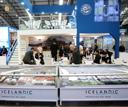 Exhibition booth featuring a blue backdrop, showcasing Icelandic products and attendees engaged in discussion.