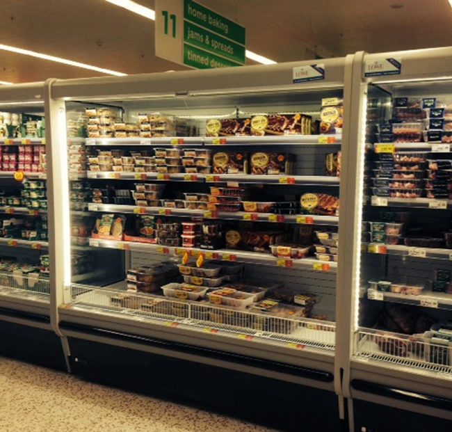 Chilled display cabinet filled with various packaged food items, featuring bright lighting and glass doors.