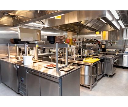 Modern stainless steel kitchen with various cooking equipment and utensils, featuring bright overhead lighting.
