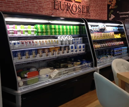 Chilled display case filled with colourful beverages and dairy products against a brick wall backdrop.