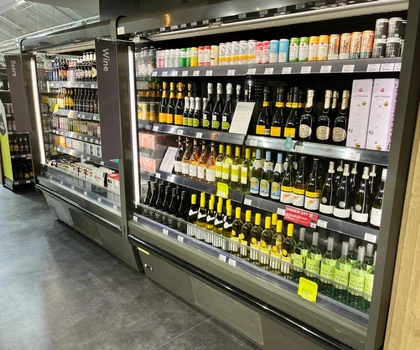 A well-stocked beverage fridge displaying various wine bottles in shades of green, gold, and black.