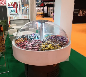A clear display case filled with colourful candies, set against a bright exhibition backdrop.