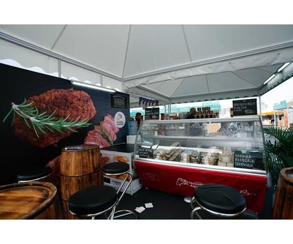 A food stall featuring a red counter, wooden barrels, and a large meat display backdrop.