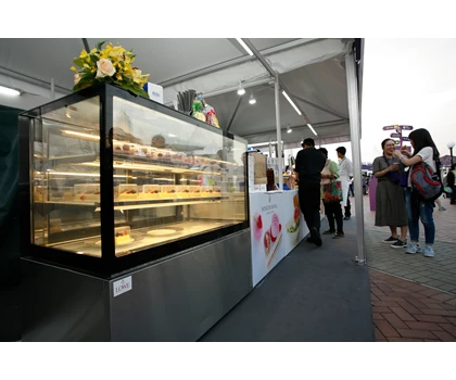 A glass display case filled with pastries, surrounded by festival attendees in a tented area.