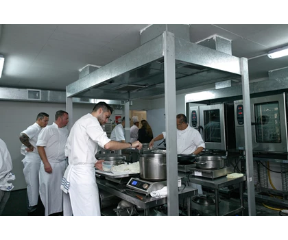 Chefs in white uniforms prepare food in a modern kitchen with stainless steel equipment.