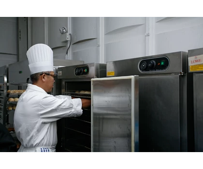 A chef in a white uniform and tall hat reaches into a stainless steel oven.