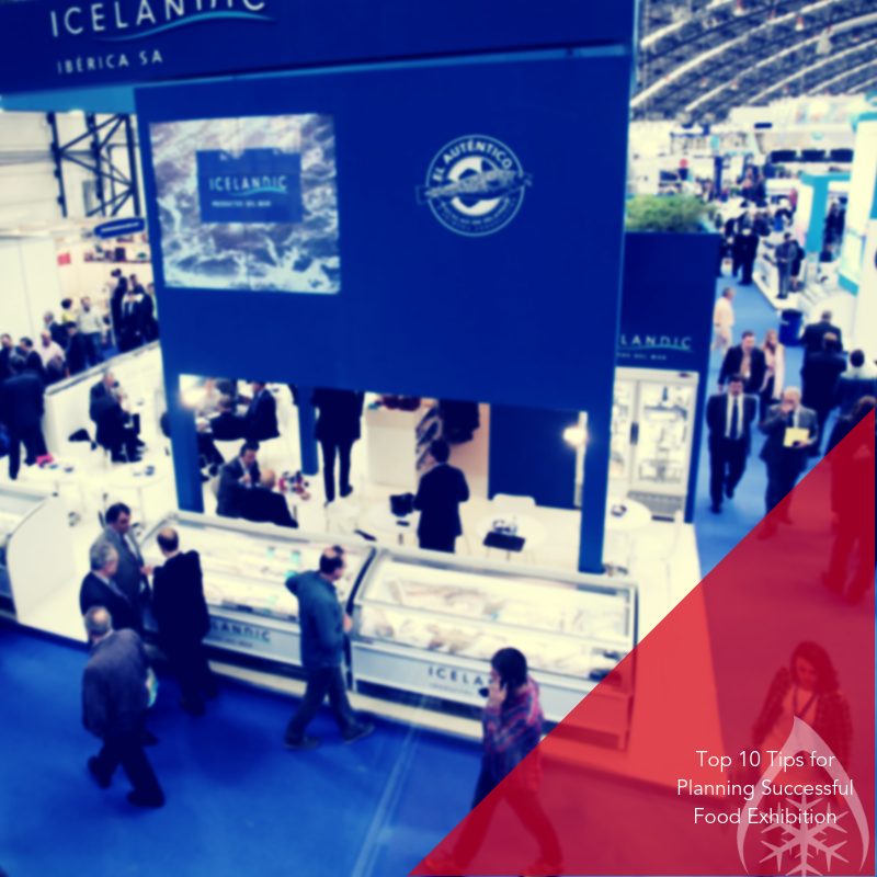 Busy food exhibition featuring a blue and white booth with people interacting and browsing displays.